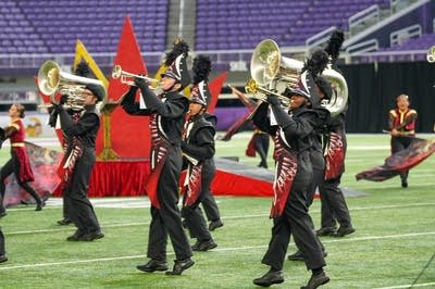 A marching band performs on the field of a football stadium.