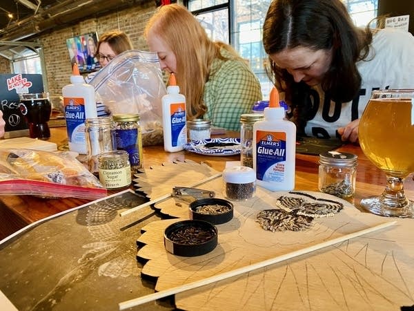 People gather around a wooden table inside a brewery to create crop art.