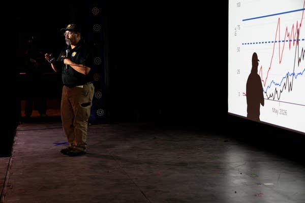 A man talks on stage with a presentation