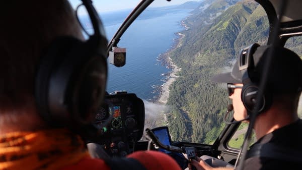 Two men in a helicopter over an Alaskan beach.