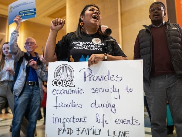 A woman holds a sign and leads a chant