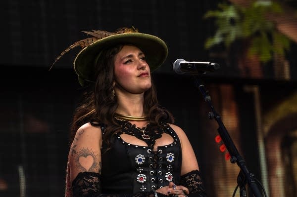 A woman in a stylish hat sings on a large outdoor stage