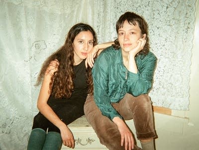 Two women sit on a dresser to pose for a photo
