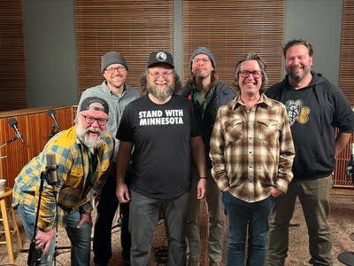 Six men stand together for a group photo in a recording studio
