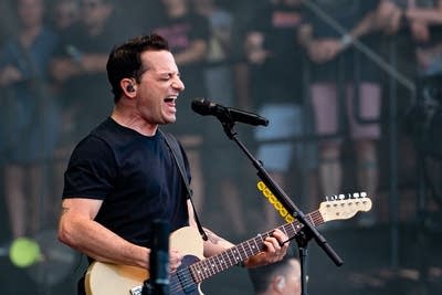 A man sings and plays guitar on a large outdoor stage