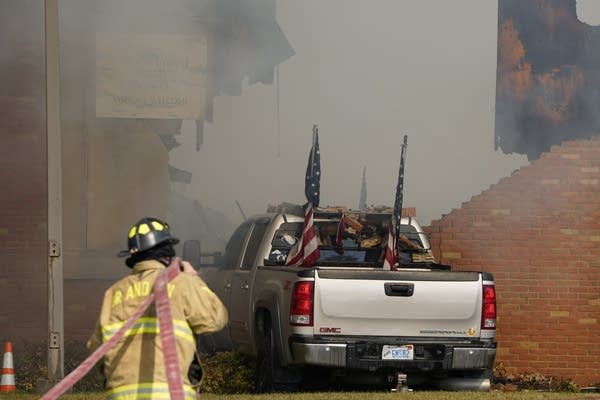 A silver truck with American flags in the bed is crashed into a smoking brick wall.