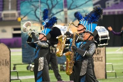 A marching band performs on the field of a football stadium.