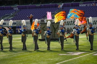 A marching band performs on the field of a football stadium.