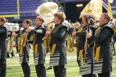 A marching band performs on the field of a football stadium.