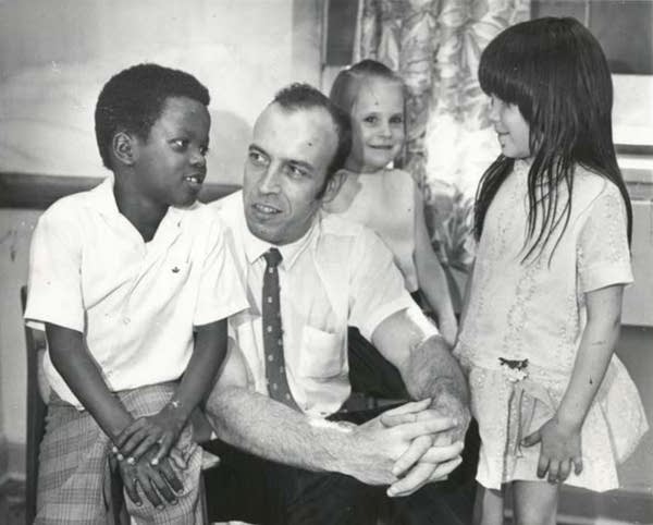 A man in a white shirt and tie is surrounded by three students.