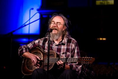 A musician sings and plays a resonator guitar onstage at a music festival