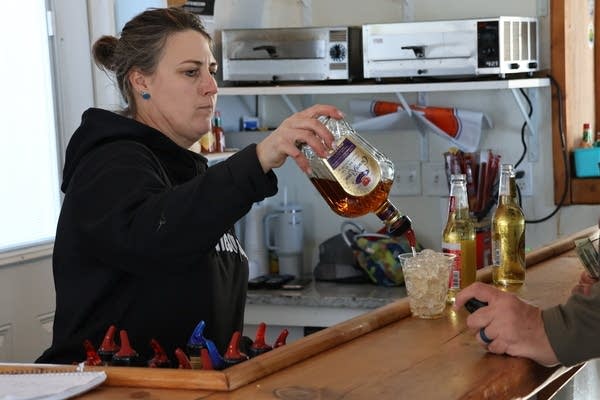 A bartender pours a drink into a glass full of ice.