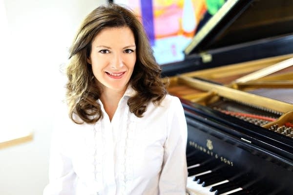 A woman sits at a piano in a sunny room
