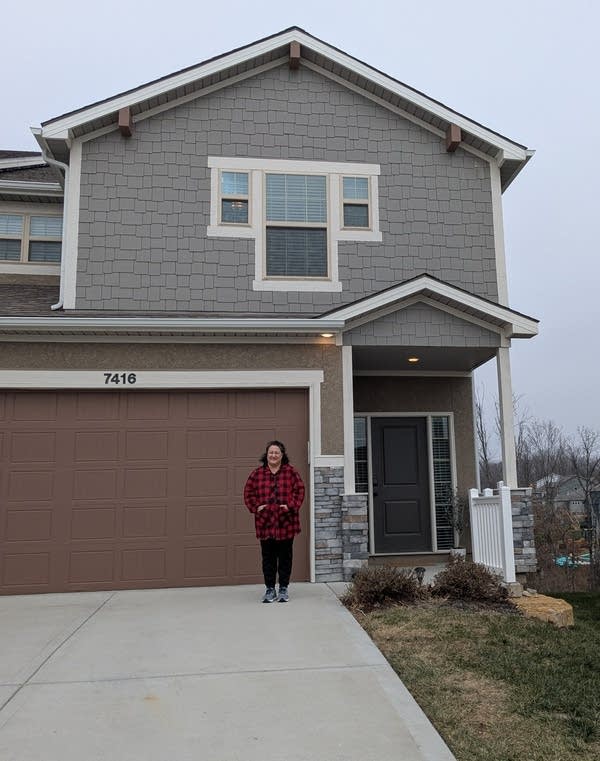 A woman in a red jacket stands in front of a townhouse and garage