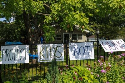 Signs hung up on a black metal fence. They read "PROTECT KIDS NOT GUNS."