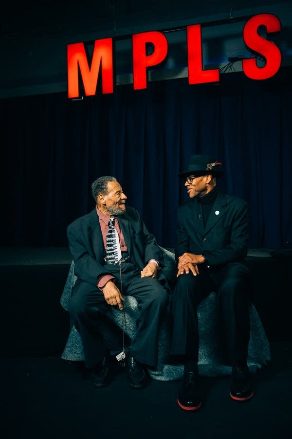 Cornbread Harris and Jimmy Jam look at each other under a red "MPLS" sign