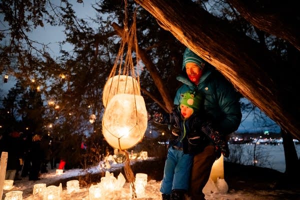 A man and toddler look at a hanging luminary made of ice.