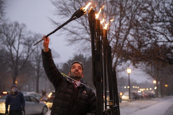 A man uses a torch to light a menorah. 