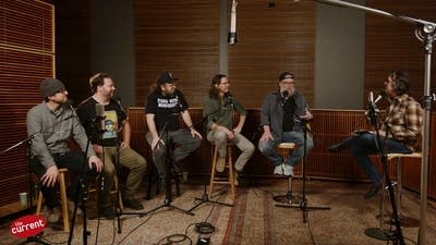 Six men have a conversation in a recording studio