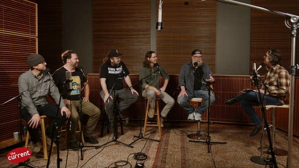 Six men have a conversation in a recording studio