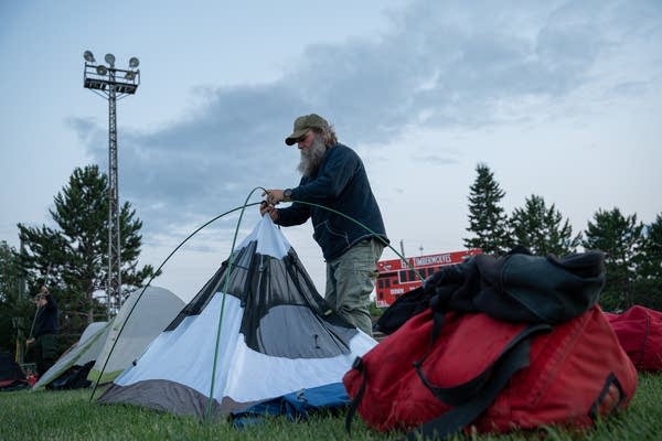 A man pitches a tent on a high school football field.
