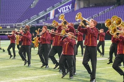 A marching band performs on the field of a football stadium.