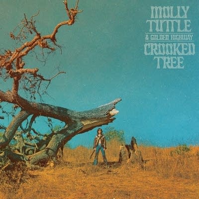A woman with a guitar standing by a crooked, twisted, broken tree