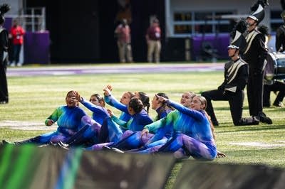 A marching band performs on the field of a football stadium.