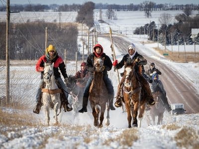 Riders on horseback crest a snowy hill