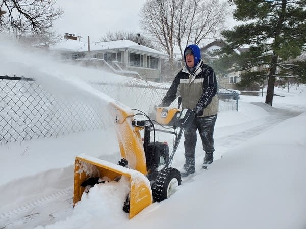 A man snowblows a sidewalk