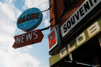 A circular sign reading 'Globe' above an arrow-shaped sign reading 'News' mounted to the corner of a brick building