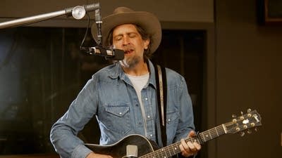 A musician sings and plays guitar in a recording studio
