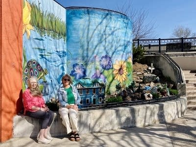 Two people sit near a stairwalk and sidewalk, with a painting.