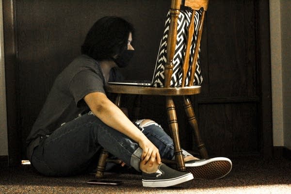 A person sits on the floor and looks at a laptop in a chair. 