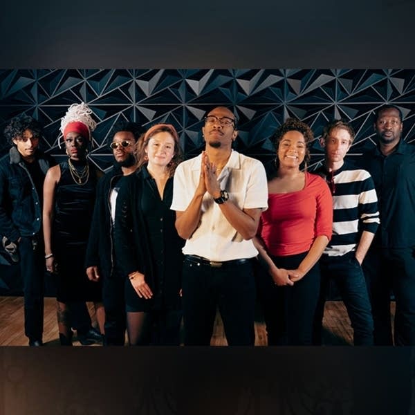 8 artists stand in front of a patterened wall