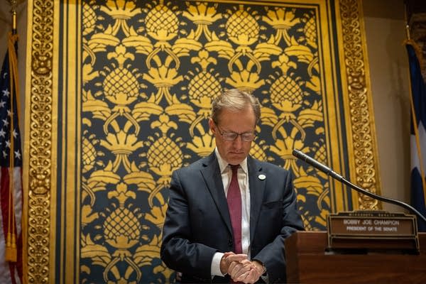 A man clasps his hands and looks down