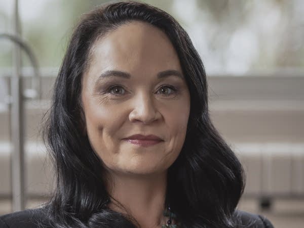 A woman in a blazer and beaded necklace smiles.