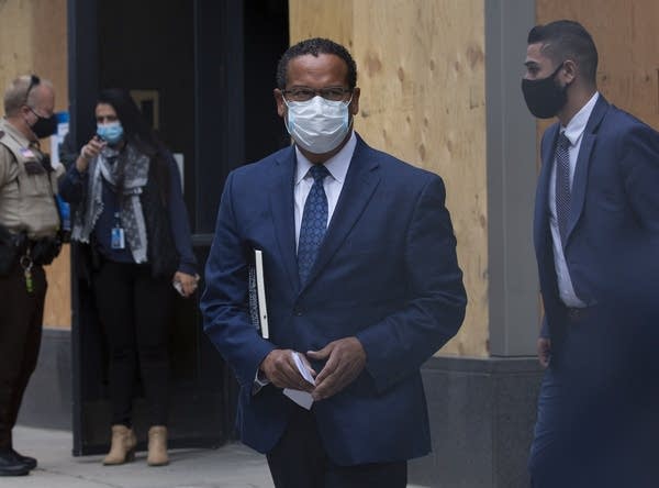 A man wearing a suit and face mask walks out of a building