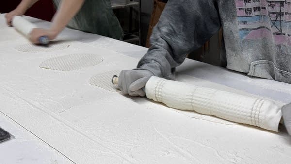 Two bakers roll out potato dough with rolling pins about two feet long.