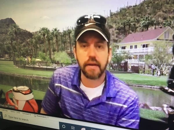 a man in a hat and sunglasses sits in front of a photo of a golf course