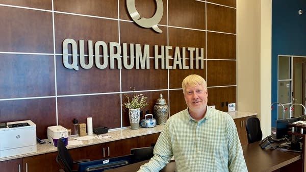A man stands near a sign that reads "Quorum Health"