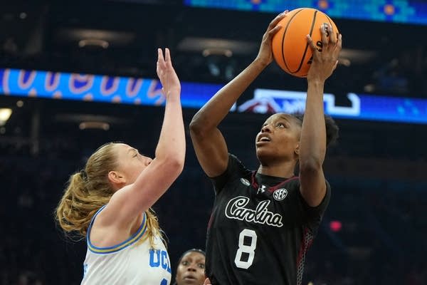 A UCLA player jumps to block a shot by a South Carolina player holding the basketball.