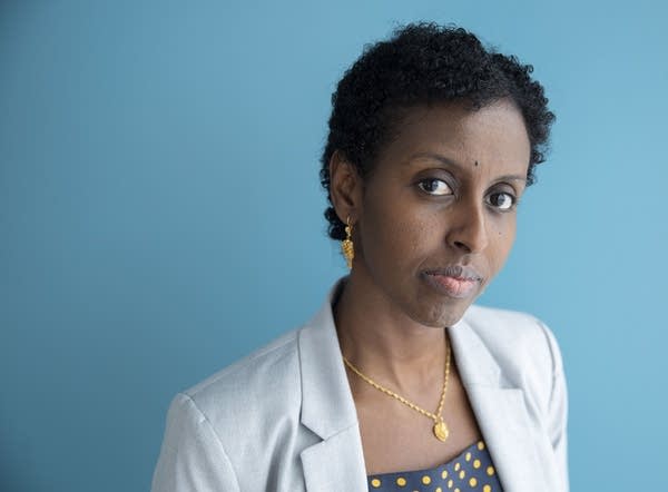 A woman wearing a gray blazer in front of a blue wall.