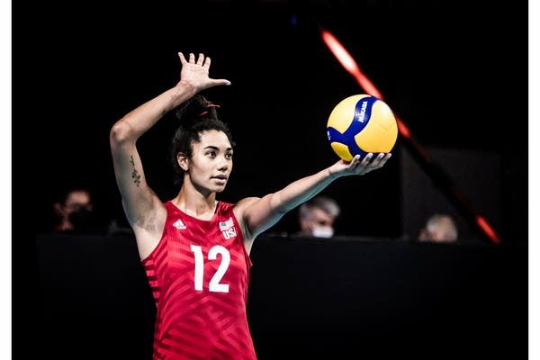A woman holds a ball up with her other hand prepared to hit the ball.