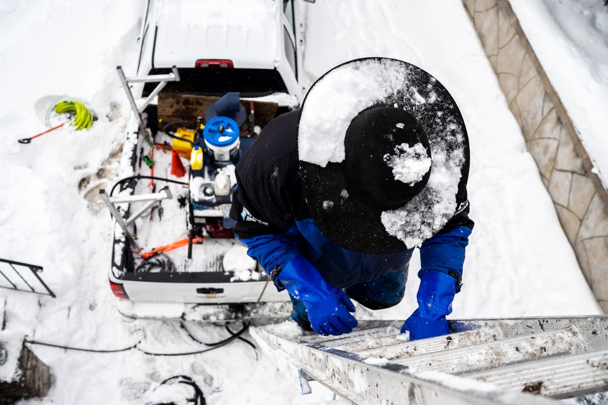 Snow falls on Jake Weber's cowboy hat as he climbs a ladder.