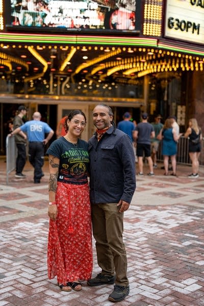 Two music fans pose for a portrait outside a large venue