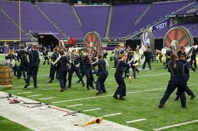 A marching band performs on the field of a football stadium.