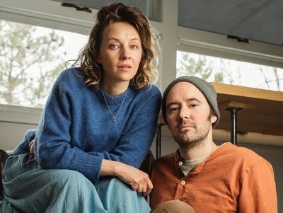 Two people in casual clothes sit together in a bright room