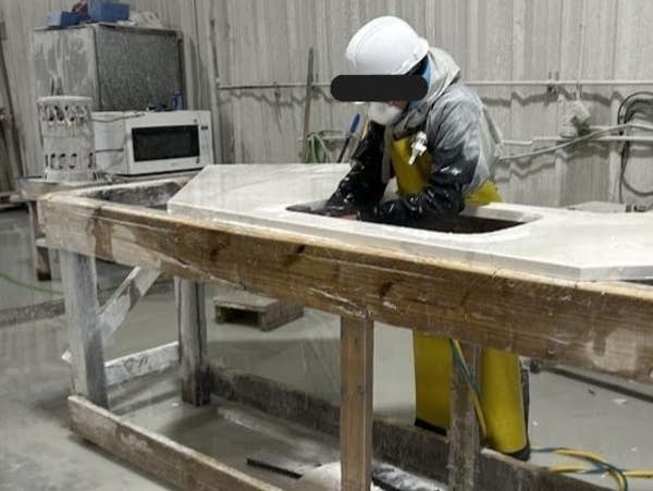 A person wearing a mask and protective suit cuts into a slab of artificial stone