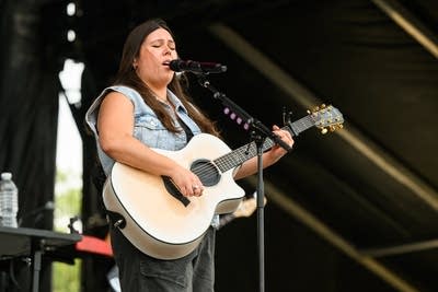 A musician sings and plays guitar on a large outdoor stage